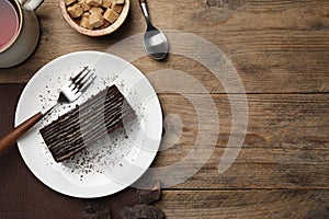 Plate with tasty Spartak cake and fork on wooden table, top view. Space for text