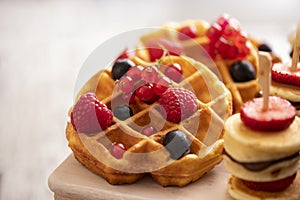 Plate with tasty waffles, fruit, and berries on grey background