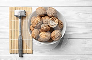 Plate with tasty walnuts and hammer on white wooden table