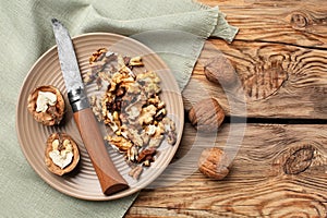 Plate with tasty walnuts and knife on wooden table