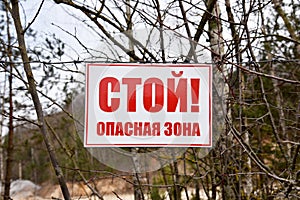 A plate with the text in Russian: Stop! Exclusion zone! Banner on barbed wire in dangerous and protected area. Stop forbidden sign