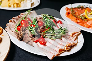 Plate of thin sliced ham and roast beef meat with red hot peppers and cherry tomatoes