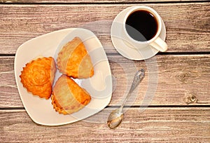 A plate with three curd buns and a cup of black coffee on a saucer, stand on a wooden table