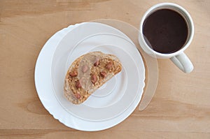 A plate with toasted bread and peanut butter and a cup of coffee on the wooden table. Top view