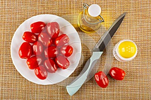 Plate with tomato cherry, bottle with vegetable oil, knife,  salt shaker on brown mat. Top view