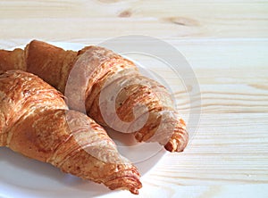 Plate of two fresh butter Croissant pastries served on light color wooden table