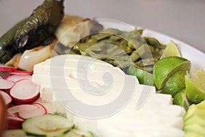 Plate of typical Mexican snack with cheese, nopales, chili peppers, avocado accompanied by a clay plate with pot beans