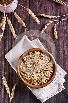 A plate with unpeeled oat seeds and ears of oats on a wooden table. Top and vertical view