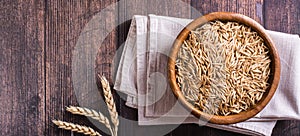 A plate with unpeeled oat seeds and ears of oats on a wooden table. Top view. Web banner