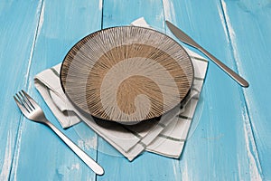 Plate with utensils and dish towel on blue wooden background with perspective