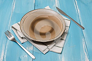 Plate with utensils and dish towel on blue wooden background with perspective