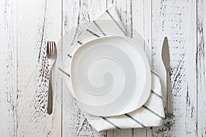 Plate with utensils and dish towel on white wooden background