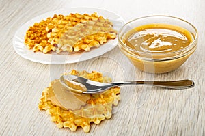 Plate with waffle, bowl with peanut butter, spoon with peanut paste on soft waffle on table