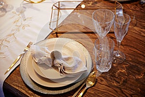 A plate on which lies a white napkin, empty glass goblets on a wooden table