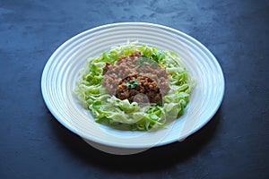 Plate of zucchini spaghetti with beef bolognese on black background.