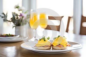 plated eggs benedict beside a mimosa on a brunch table setting