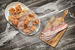 Plateful of Cheese Pie Slices and Cutting Board with Pork Bacon Rashers Set on Old Garden Table photo