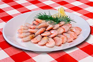 Plateful of cooked shrimps with lemon slice on checked tablecloth