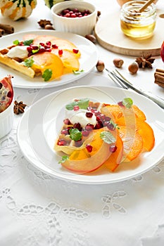 Plates of Belgian waffles with persimmon, pomegranate seeds and sour cream