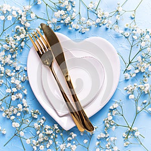 Plates in form of hearts, golden knife and fork and fresh white gypsofila flowers photo