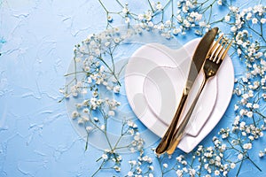 Plates in form of hearts, golden knife and fork and fresh white gypsofila flowers photo