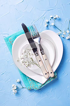 Plates in form of hearts, napkin, knife and fork and fresh white gypsofila flowers photo