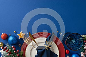 Plates, golden utensils, napkin ring, glass, shimmering balls, star candle, confetti, frosted fir twigs, berries on blue backdrop