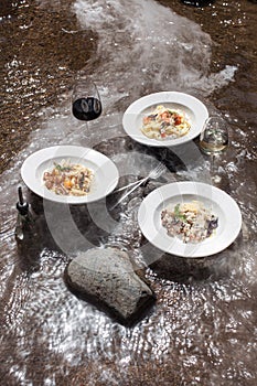 Plates of italian pasta on river with smoke in forest sunlight flares top