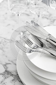 Plates with knives forks on white marble table, closeup