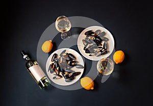 Plates with mussels, bottle of white wine and glasses of white wine on dark background