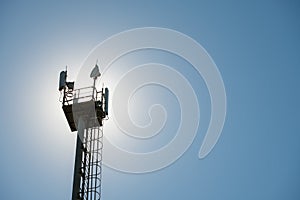 Platform on a cell phone mast with fences and transmitters, against the backdrop of the sun on a summer day