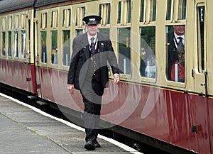 Platform guard walking alongside train carriages at Grosmont station, North Yorkshire Moors, UK