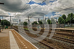 Platform, railroad rails and signaling at train station under blue cloudy sky at Weesp.