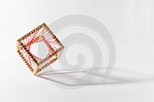 Platonic solid wooden cube with red thread on edge over white background