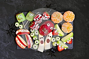 Platter of healthy Halloween fruit snacks, top view over a black stone background.