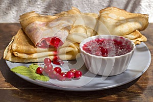 A platter of red currant jam and thin folded pancakes on a plate. Traditional Russian food