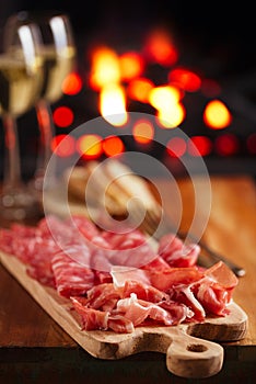 Platter of serrano jamon Cured Meat with cozy fireplace and wine