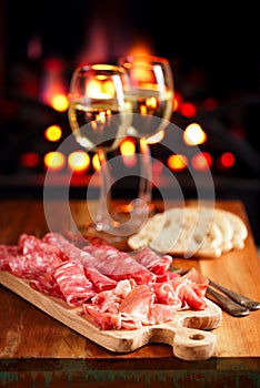 Platter of serrano jamon Cured Meat with cozy fireplace and wine