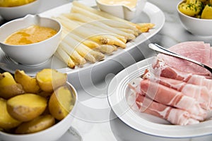 Platter white German asparagus with potatoes, cooked and smoked ham, Sauce Hollandaise and melted butter on marble background