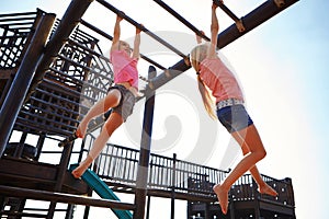 Play fills your body with health. two little girls hanging on the monkey bars at the playground.