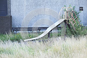 Play park derelict abandoned slide in overgrown grass at playground