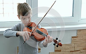 Play the violin. Seven years old boy playing the violin near a window. Front view.