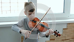 Play the violin. Seven years old boy playing the violin near a window. Front view.