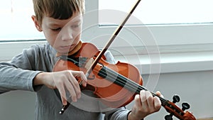 Play the violin. Seven years old boy playing the violin near a window. Front view.