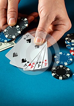 The player bets on a winning combination four of a kind or quads in poker game on a blue table with chips and money in casino.