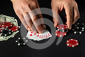 The player bets on a winning combination royal flush in poker game on a black table with chips and money in a club