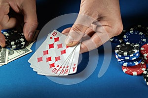 The player bets on a winning combination royal flush in poker game on a blue table with chips and money in a club