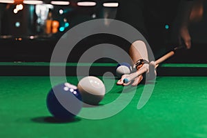 Player holding que and aiming to billiard white ball. White ball on green poll table