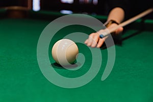 Player holding que and aiming to billiard white ball. White ball on green poll table