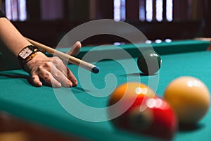 Player holding que and aiming to billiard white ball. White ball on green poll table